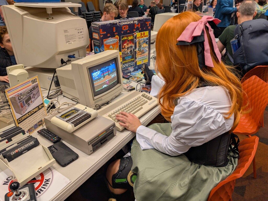 Orange hair and a pink bow, playing a Commodore 64 at a retro computing event
