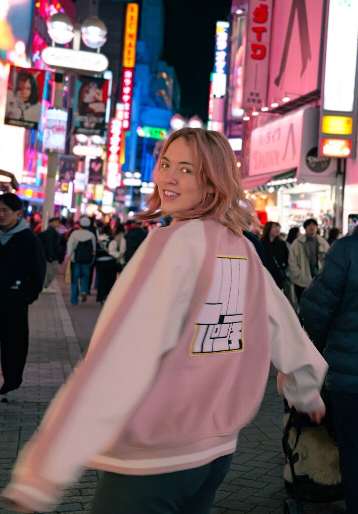 Freesia looking back on a neon street, pink and white jacket, hair moving