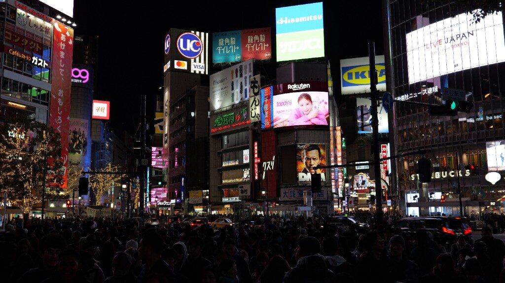 A crowded crossing at night under huge illuminated billboards