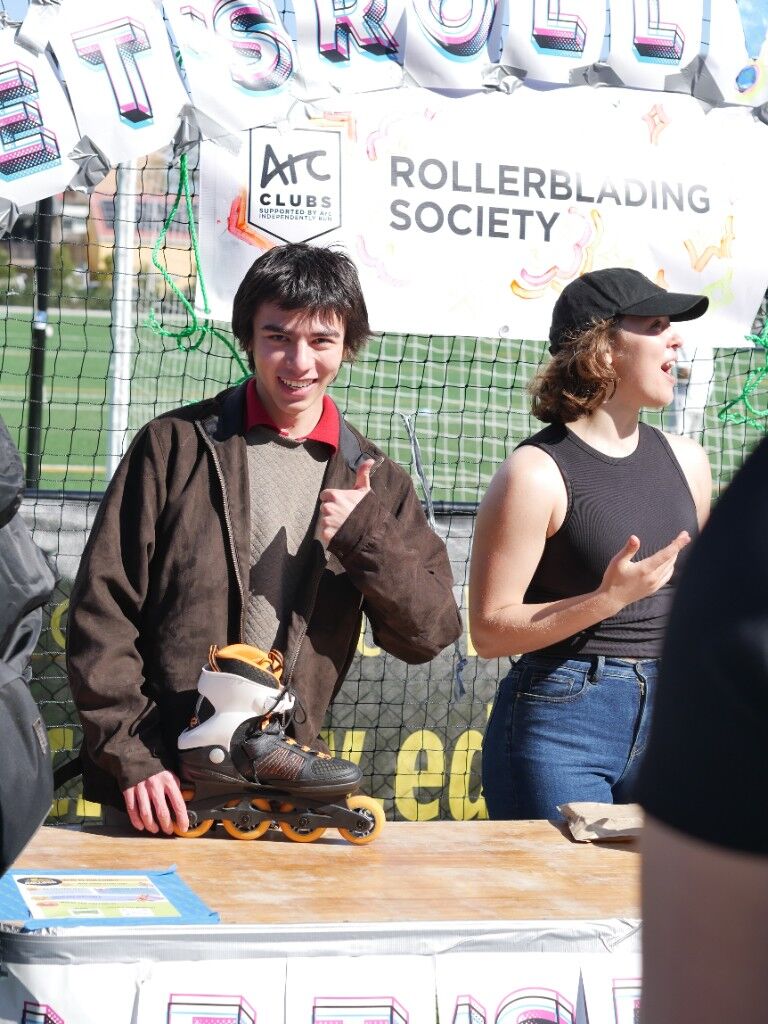 A sunny stall for a rollerblading society, a skate on the table, two people behind it