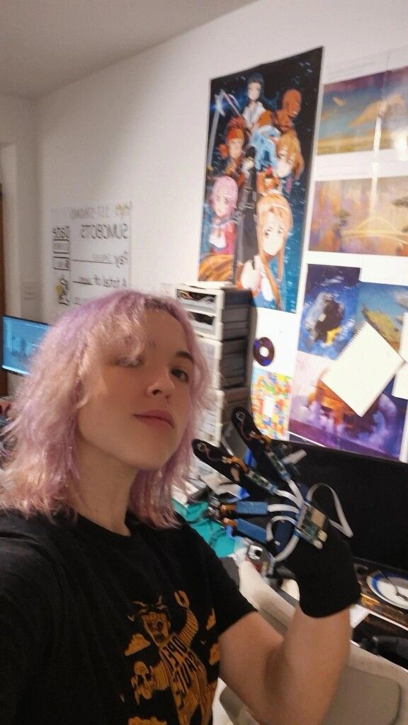 Pink hair, holding up a wired glove in a room of posters
