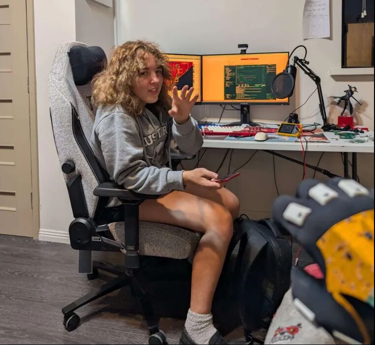 In a desk chair, two monitors of code behind her, a glove in the foreground
