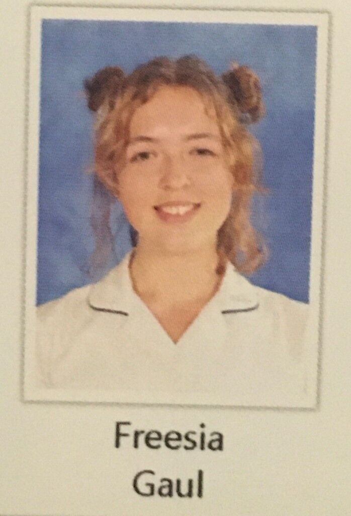 A school photo: Freesia Gaul, hair in two buns, white collar, blue backdrop