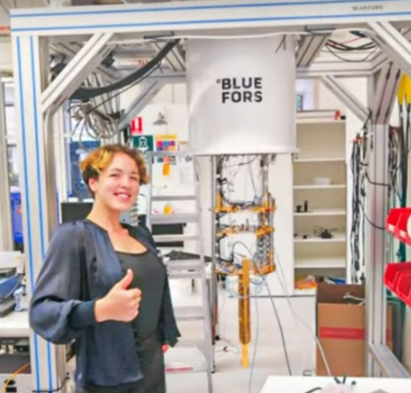 Thumbs up beside a Blue Fors machine in a lab of cables and shelves
