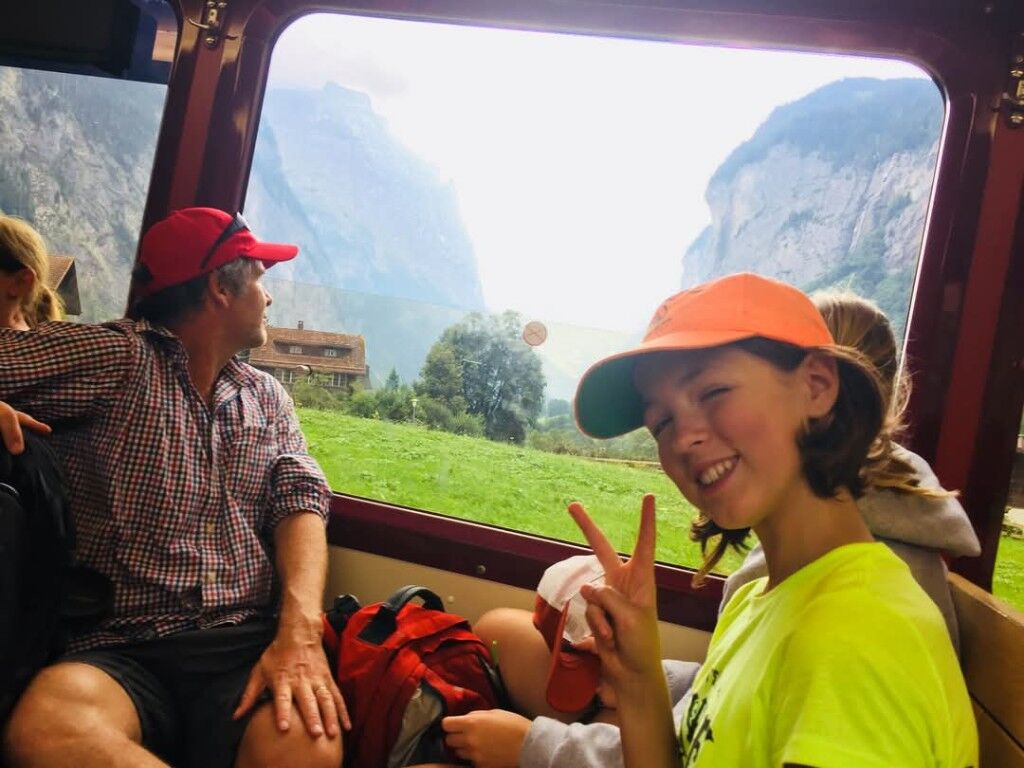 A train window on green mountains, a peace sign in an orange cap