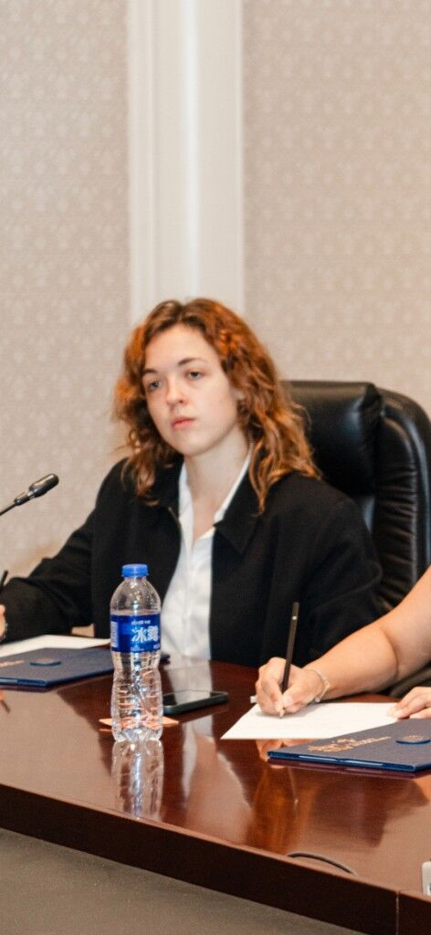 At a polished table with a microphone, a water bottle, and blue folders