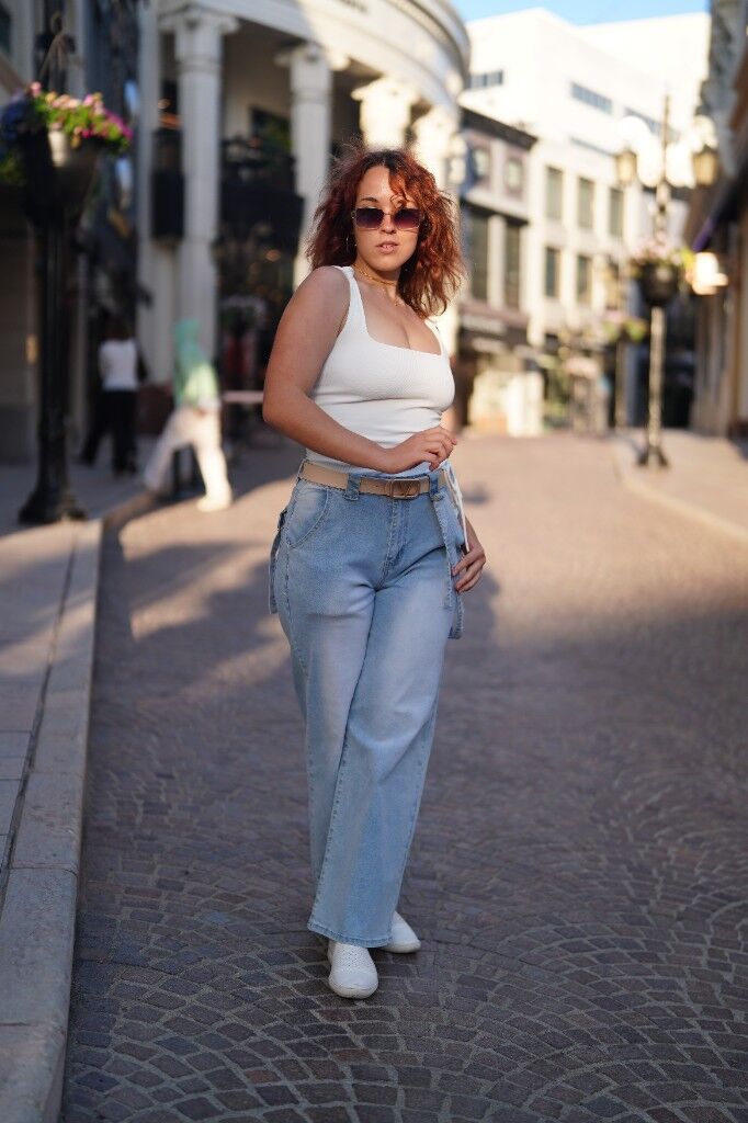 Walking a cobbled street in a white top, wide jeans, and sunglasses