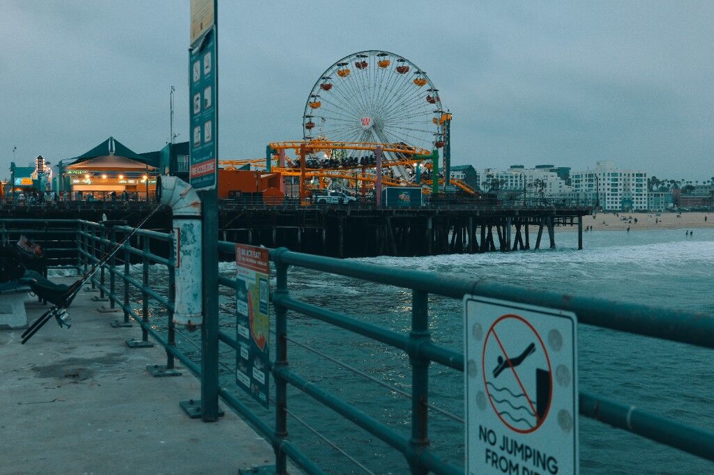 A pier in grey weather, a ferris wheel, and a sign saying no jumping