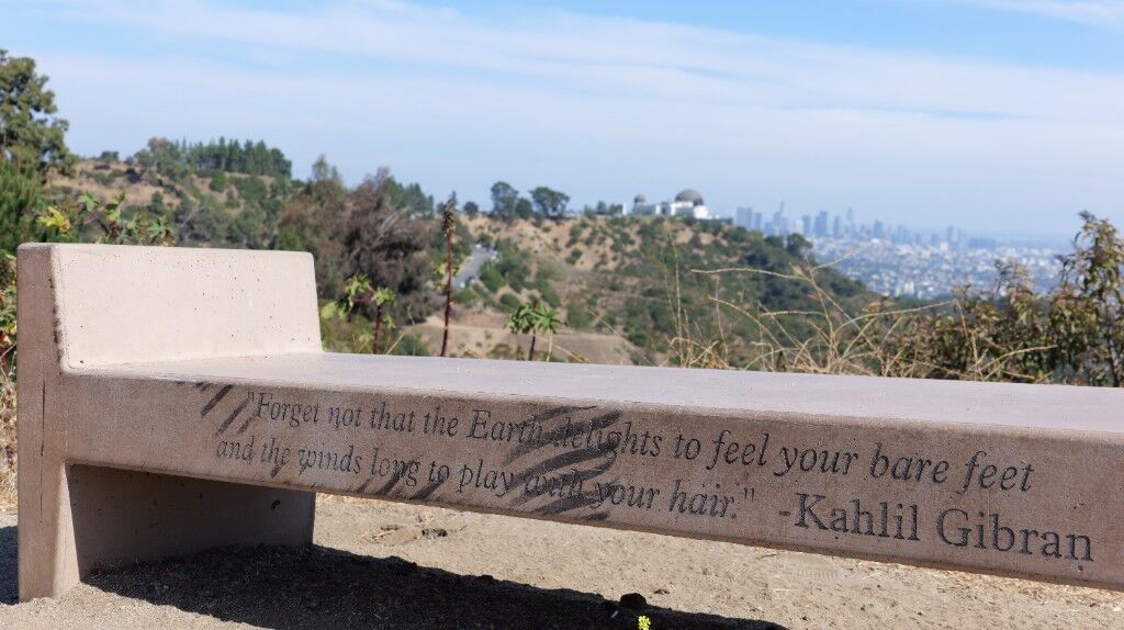 A concrete bench with a Kahlil Gibran line, city and hills behind it